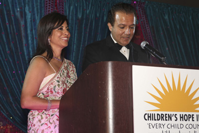 Poonam smiling beside AJ Khubani as he speaks at the Children’s Hope India gala