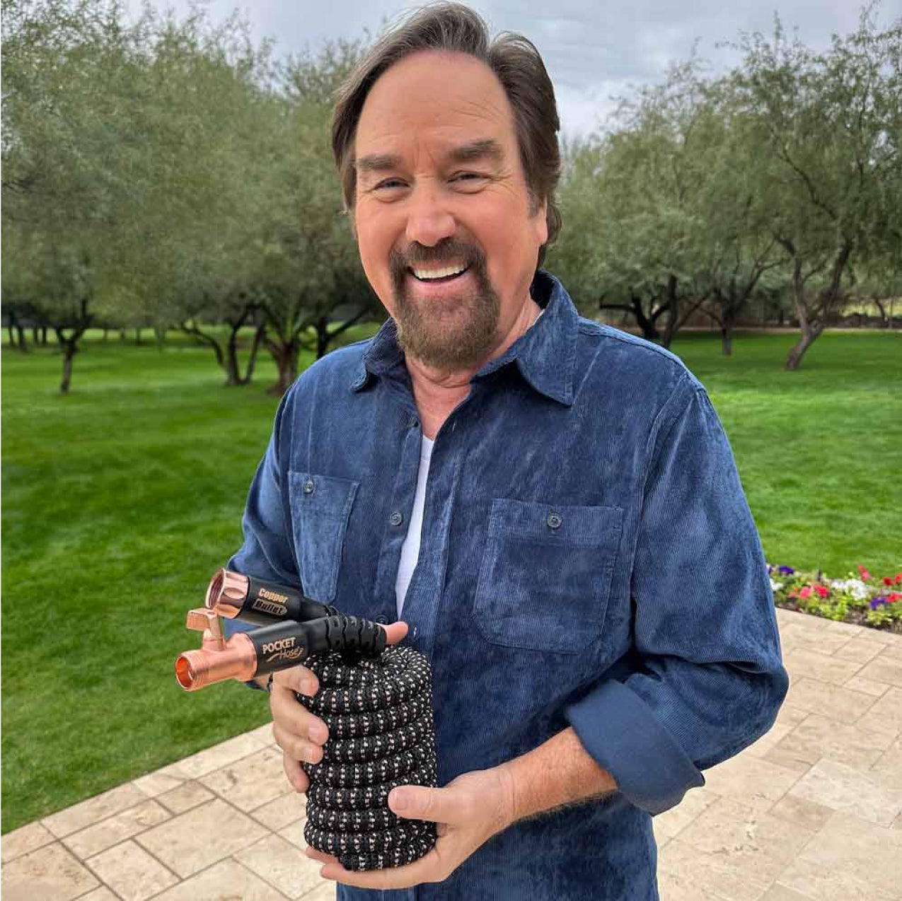Richard Karn holding a coiled Pocket Hose Copper Bullet outdoors